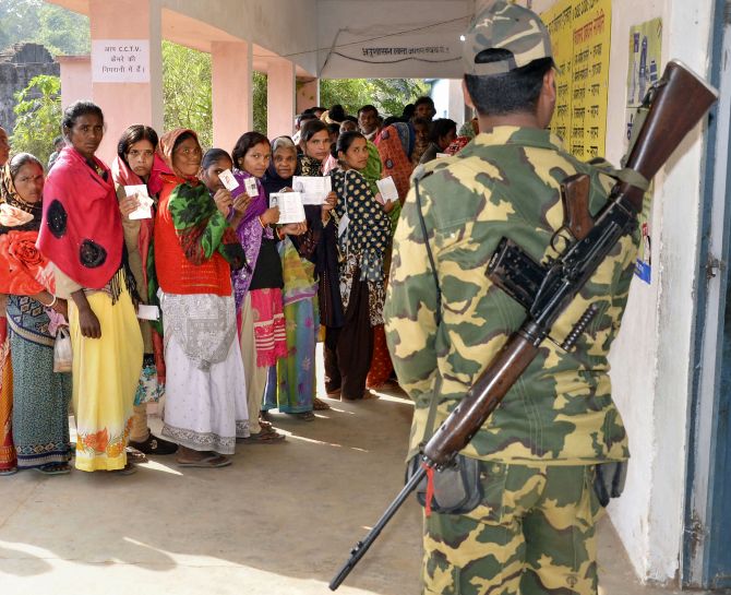 A security jawan guards as people wait in queues to cast their votes at a polling station during the second phase of Jharkhand Assembly elections at Bundu, 45 kms from Ranchi, Saturday, Dec. 7, 2019. (PTI Photo)