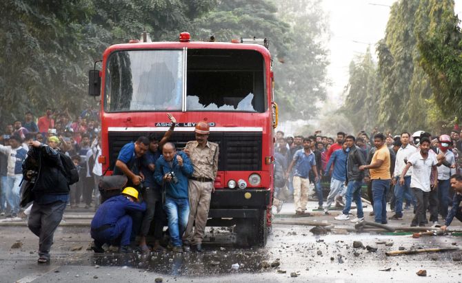 Media person and Firefighters find shelter in front of a fire brigade vehicle as demonstrators vandalise it during a protest against the Citizenship (Amendment) Act 2019 in Guwahati . Photograph:ANI Photo