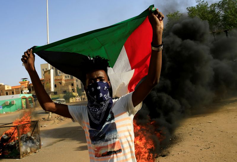 A protester carries a Sudanese national flag as he burns tyres during a demonstration against a report of the Attorney-General on the dissolution of the sit-in protest in Khartoum, Sudan July 27, 2019. REUTERS/Mohamed Nureldin Abdallah