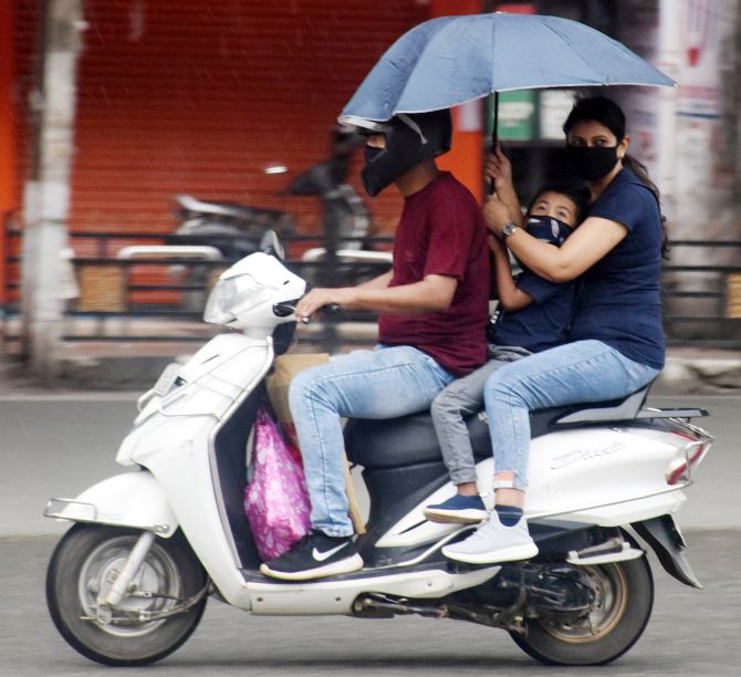  A family use umbrella to protect themselves from rain as they walk to home on a two-wheeler during the nationwide lockdown to curb the spread of coronavirus in Guwahati on Tuesday. (ANI Photo)