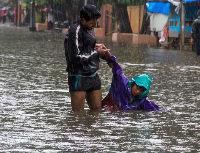Thane: A man helps a child to stand at a flooded road following heavy monsoon rains, in Thane, Sunday, Aug 4, 2019. (PTI Photo) 
