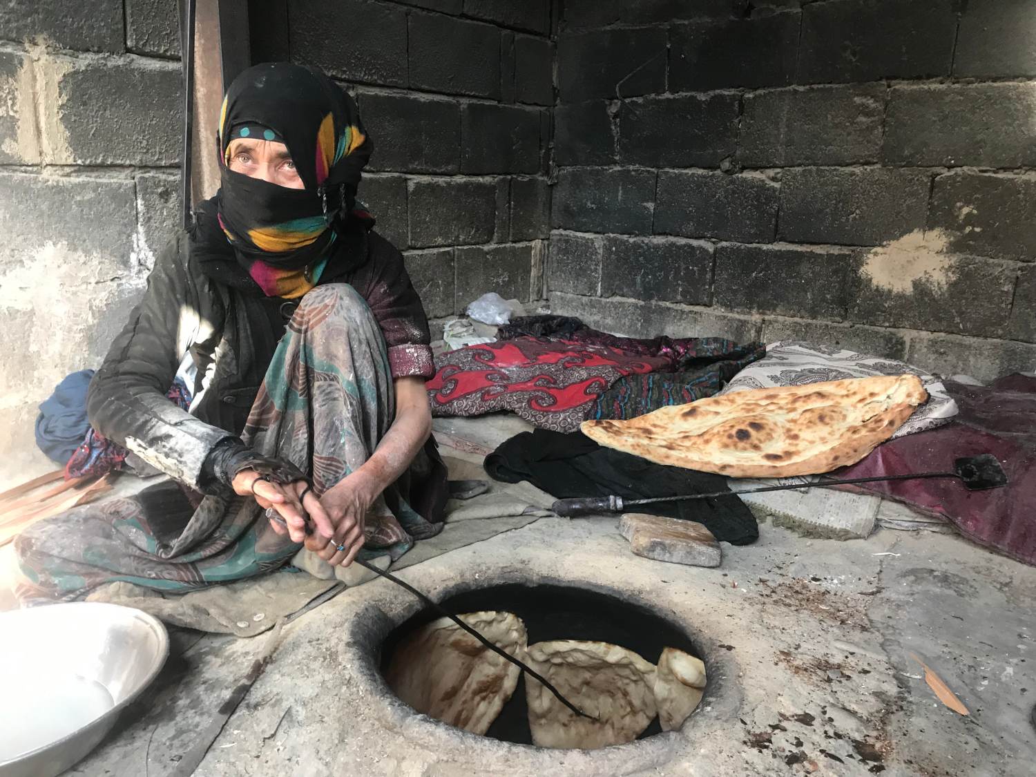 Tahera Mohamedi hunches over a tandoor oven where she bakes bread for a living in a refugee settlement near Barikab, on the outskirts of Kabul, Afghanistan. November 7, 2019. Thomson Reuters Foundation/Rina Chandran