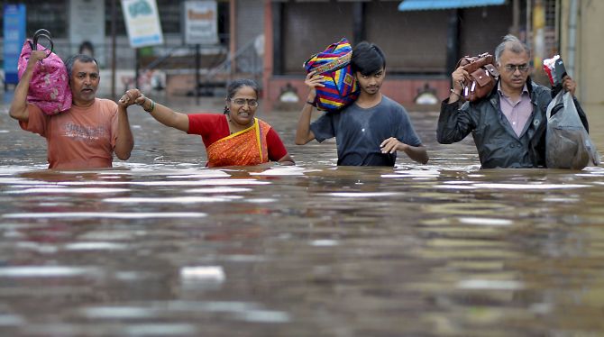 Residents wade across a flooded street with their belongings to relocate to a safer place due to overflowing Krishna river during monsoon season, in Sangli, Wednesday, Aug 7, 2019. (PTI Photo) 
