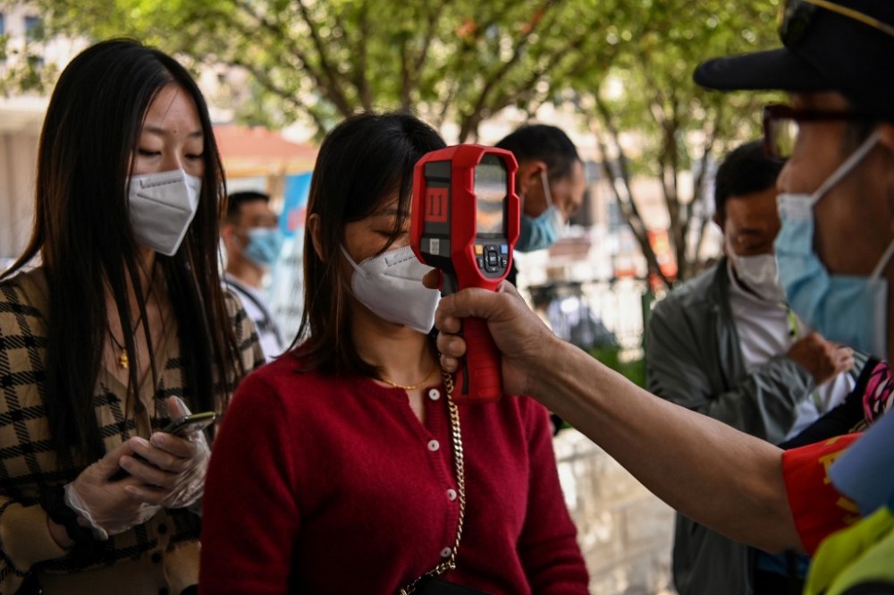 A worker wearing a face mask checks passengers body temperatures and a health code on their phones before they take a taxi after arriving at Hankou railway station in Wuhan, China's central Hubei province . Photo by Hector Retamal/AFP