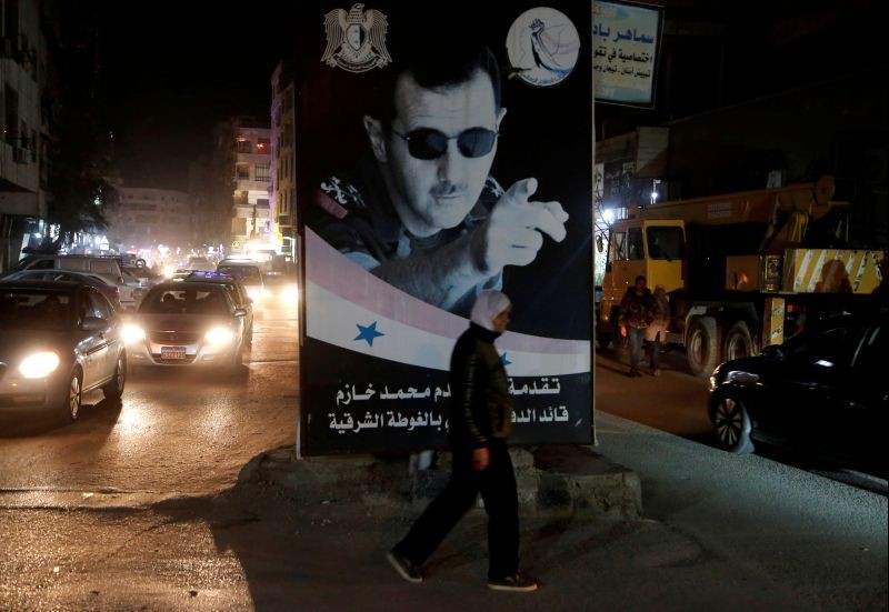 A woman walks past a poster depicting Syria's President Bashar al-Assad in Damascus, Syria on March 5, 2020. (REUTERS File Photo)