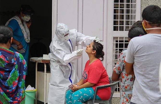 A health worker collects a sample of a woman for COVID-19 test via Rapid Antigen at Chakkarpur Community Centre, in Gurugram, on Friday. Photograph: PTI Photo