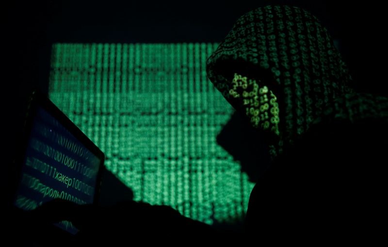 A hooded man holds a laptop computer as cyber code is projected on him in this illustration picture. (REUTERS File Photo)