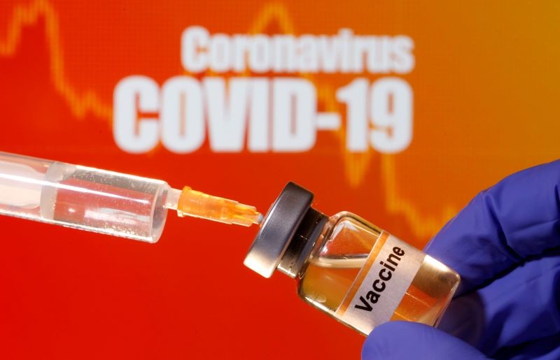 A small bottle labeled with a "Vaccine" sticker is held near a medical syringe in front of displayed "Coronavirus COVID-19" words in this illustration taken on April 10, 2020. (REUTERS File Photo)