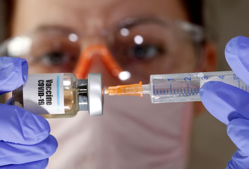 A woman holds a small bottle labeled with a "Vaccine COVID-19" sticker and a medical syringe in this illustration taken April 10, 2020. REUTERS/Dado Ruvic/Illustration/File Photo