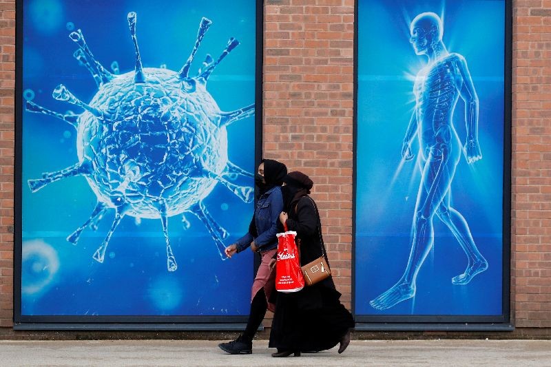 People walk past an illustration of a virus outside a regional science centre, as the city and surrounding areas face local restrictions in an effort to avoid a local lockdown being forced upon the region, amid the coronavirus disease (COVID-19) outbreak, in Oldham, Britain August 3, 2020. REUTERS/Phil Noble