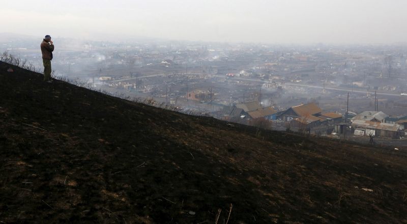FILE PHOTO: A man looks downhill at the settlement of Shyra, damaged by recent wildfires, in Khakassia region, April 13, 2015. Wildfires in the Russian region of Khakassia in southern Siberia have killed 15 people and caused damage worth at least $96 million, the region's leader said on Monday. REUTERS/Ilya Naymushin/File Photo