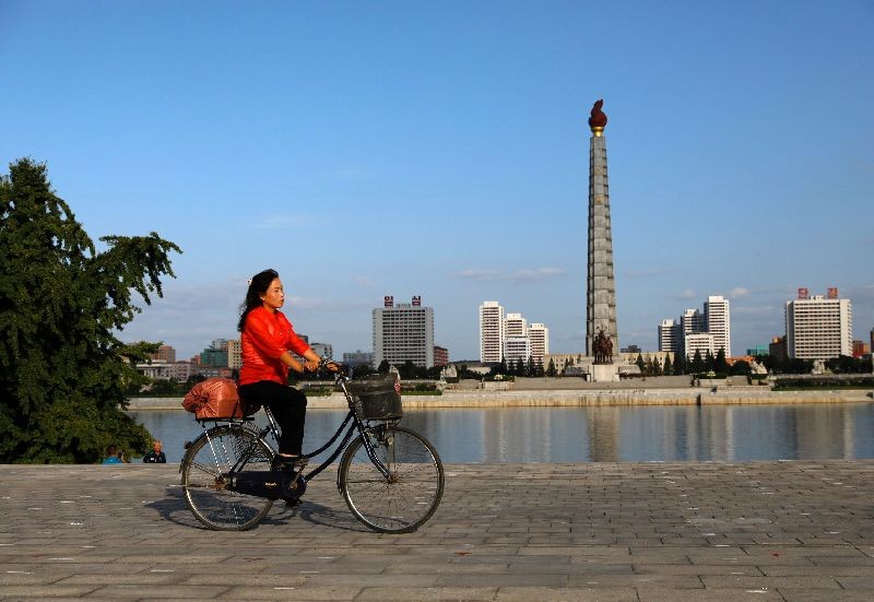 FILE PHOTO: A woman rides a bicycle as Juche Tower is seen in the background along the Taedong river in Pyongyang, North Korea, September 12, 2018. REUTERS/Danish Siddiqui/File Photo