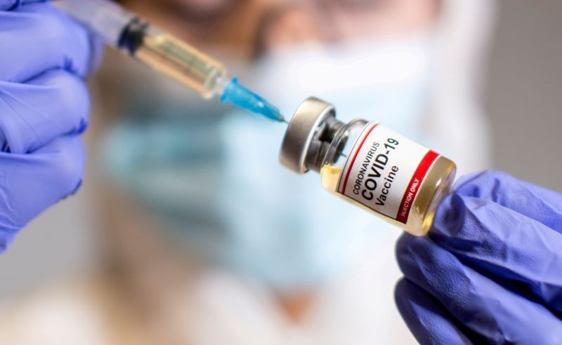 A woman holds a small bottle labeled with a "Coronavirus COVID-19 Vaccine" sticker and a medical syringe in this illustration taken October 30, 2020. REUTERS/Dado Ruvic/File Photo