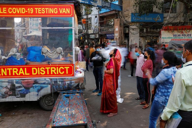 A healthcare worker wearing personal protective equipment (PPE) collects a swab sample from a woman amidst the spread of the coronavirus disease (COVID-19), at a wholesale market, in the old quarters of Delhi, India, November 17, 2020. Picture taken with slow shutter speed. REUTERS/Adnan Abidi
