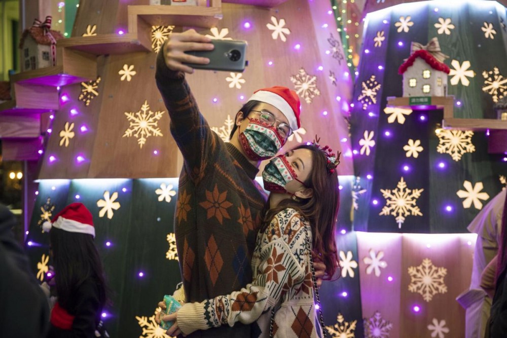 A couple wearing protective masks to prevent the spread of coronavirus, take a selfie in front of Christmas decorations in Hong Kong, Thursday, Dec. 24, 2020. (AP Photo/Kin Cheung)