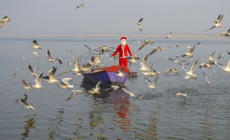 Mirzapur: A man dressed as Santa Claus feeds gulls at River Ganga on the occasion of Christmas festival in Mirzapur, Friday, Dec. 25, 2020. (PTI Photo)