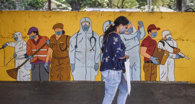 A woman, wearing a face mask, walks past a coronavirus theme-based mural, in Mumbai. Photograph: Kunal Patil/PTI Photo