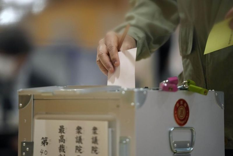 A voter casts a ballot in the lower house elections as representatives of a local election administration commission observes at a polling station on October 31, 2021, in Tokyo. (AP Photo)