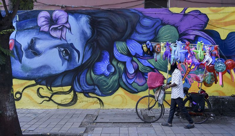 A balloon seller with a bicycle, walks past a graffiti in Mumbai on November 8, 2021. (PTI Photo)