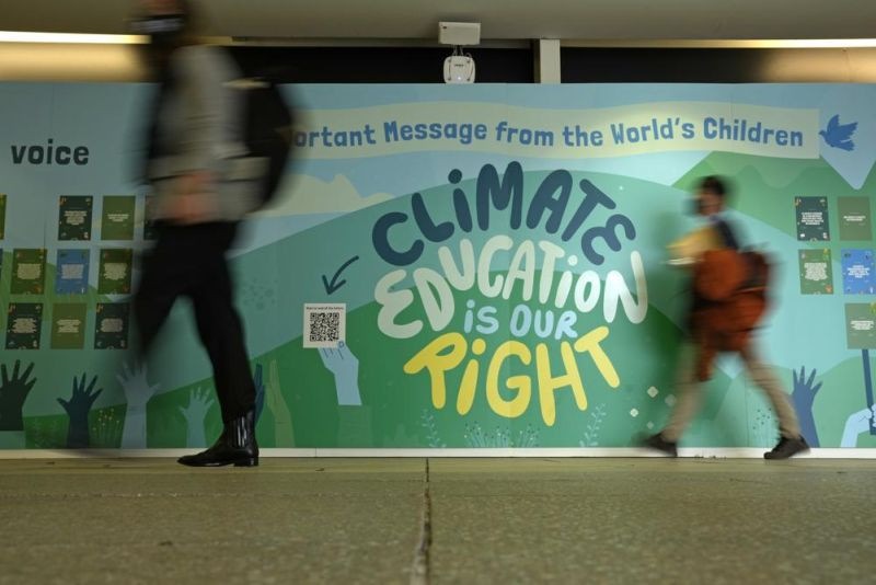 People walk past a wall with a message on climate eduction at the COP26 U.N. Climate Summit in Glasgow, Scotland, Sunday, Oct. 31, 2021. The U.N. climate summit in Glasgow formally opens Sunday, a day before leaders from around the world gather in Scotland's biggest city to lay out their vision for addressing the common challenge of global warming. (AP Photo)