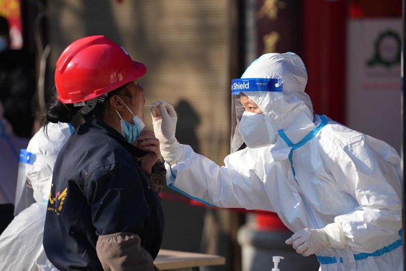 In this photo released by China's Xinhua News Agency, a worker wearing a protective suit collects a throat swab sample at a COVID-19 testing site in Xi'an in northwestern China's Shaanxi Province, Tuesday, Dec. 21, 2021. China on Wednesday ordered millions of people locked down in neighborhoods and workplaces in the northern city of Xi'an following a spike in coronavirus cases. (AP Photo)