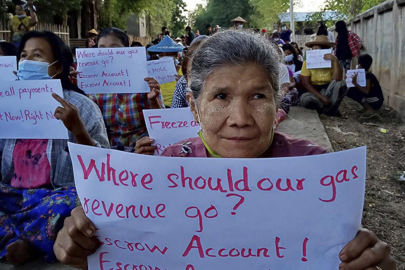 In this photo provided by Nwe Oo Tawlanyae Latpantaung, women sit in protest in the village of Latpantaung in Myanmar on Oct. 28, 2021, while holding signs calling for the freezing of revenues the Myanmar military gets from the sale of oil and gas. As the military's abuses have grown after seizing power in February, people from Myanmar's southern jungles to its northern mountains are voicing support for targeted sanctions on oil and gas funds, the country's single largest source of foreign currency revenue. (AP Photo)