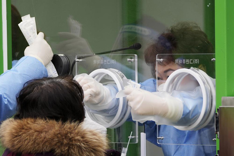 A medical worker wearing protective gear in a booth takes a sample from a woman at a temporary screening clinic for the coronavirus in Seoul, South Korea, Friday, Dec. 10, 2021. New coronavirus infections in South Korea exceeded 7,000 for the third consecutive day on Friday in a record-breaking surge that has crushed hospitals and threatens the country's goals to weather the pandemic without lockdowns. (AP Photo)