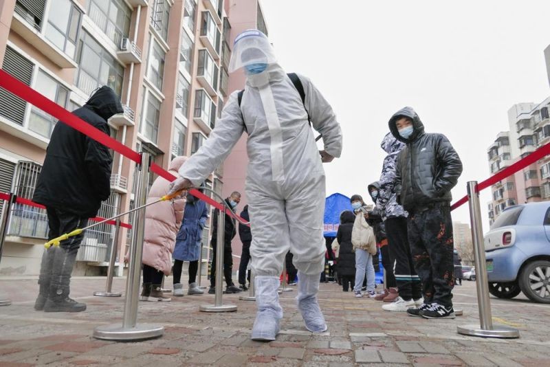 A worker wearing a protection suit sprays disinfectant as residents wearing face masks to protect from the coronavirus line up for the coronavirus test during a mass testing in north China's Tianjin municipality, Sunday, Jan. 9, 2022. The northern Chinese city of Tianjin ordered a second round of COVID-19 testing on all 14 million residents Wednesday following the discovery of 97 cases of the omicron variant during initial screenings that began Sunday. (AP File File )