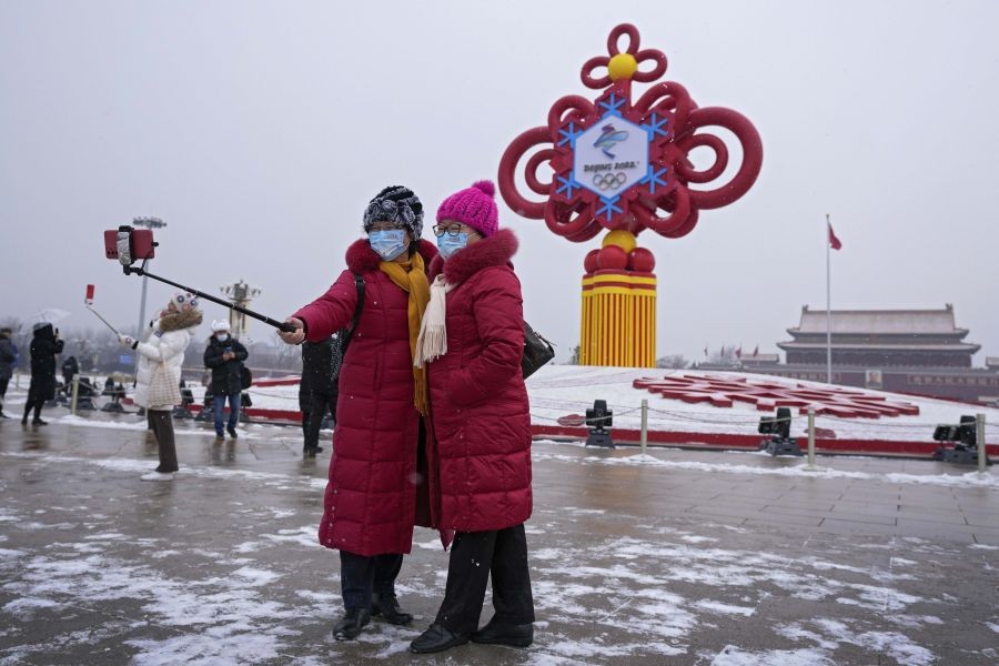 Beijing: Women wearing face masks printed with a slogan for the Beijing Winter Olympics Games take a selfie with a decoration for the Winter Olympics Games in Tiananmen Square in Beijing, Thursday, Jan. 20, 2022. With just over two weeks before the opening of the Beijing Winter Olympics, residents of the Chinese capital say they're disappointed at not being able to attend events because of coronavirus restrictions that have seen parts of the city placed under lockdown. AP/PTI