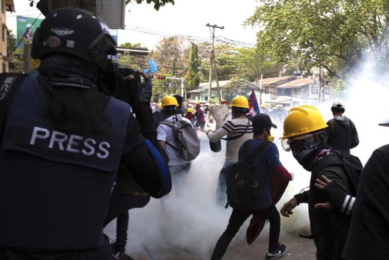 A photographer wearing a protective vest with a 'press' sign at the back films an anti-military government protest being dispersed with tear gas by security forces in Sanchaung township in Yangon, Myanmar on March 3, 2021. Since Myanmar's military dismissed the results of democratic elections and seized power on Feb. 1, 2021, peaceful nationwide protests and violent crackdowns by security forces have spiraled into a nationwide humanitarian crisis. (AP File Photo)