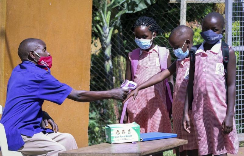 A school security guard measures the temperature of the pupils at the entrance of Kitante Primary School in Kampala, Uganda Monday, Jan. 10, 2022. Uganda's schools reopened to students on Monday, ending the world's longest school disruption due to the COVID-19 pandemic. (AP Photo)