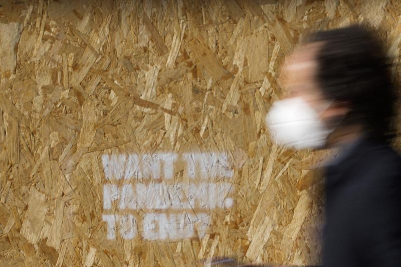 A man wearing a face mask walks past a wooden board with graffiti reading "Want the pandemic to end?" in Rome, Friday, Jan. 7, 2022. Italy is struggling with nearly daily new records of fresh infections fueled by the omicron variant. (AP Photo)