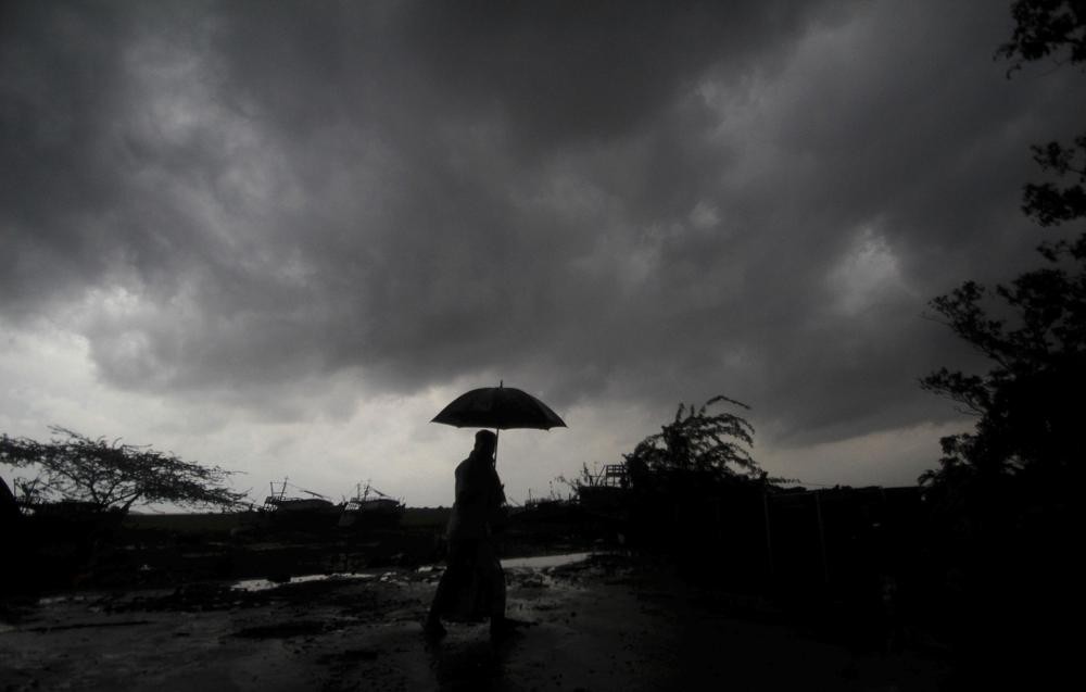 A villager holds an umbrella as dark clouds loom over Balasore district in Odisha, India, Tuesday, May 25, 2021, ahead of a powerful storm barreling toward the eastern coast. (AP File Photo)