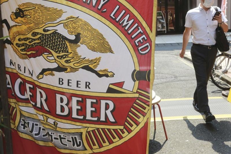 A man walks near an advertisement of a Kirin brand beer in Tokyo on Aug. 25, 2020. Japanese beverage giant Kirin Holdings said Monday, Feb. 14, 2022 it has decided to withdraw from its joint venture in Myanmar. (AP File Photo)