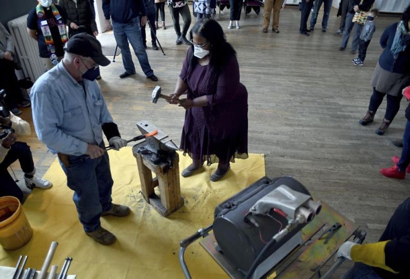 Sharletta Evans, right, whose 3-year-old son, Casson, was killed in a drive-by shooting in 1995, helps Fred Martin, a volunteer blacksmith for the nonprofit group RAWtools, hammer a rifle barrel into a garden tool at a church in Denver, Sunday, Jan. 16, 2022. (AP Photo)