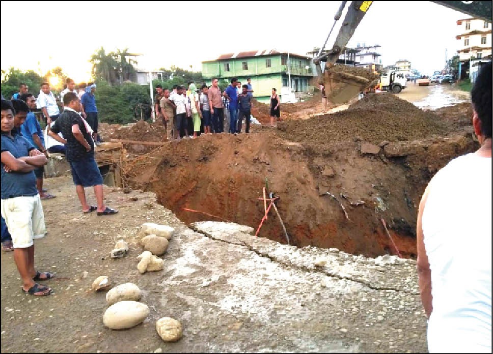 Bystanders look on as an excavator trench the road to lay a temporary drainage pipe on June 22 in the 4th Mile stretch of NH 29 before a wider ‘box culvert’ gets constructed.