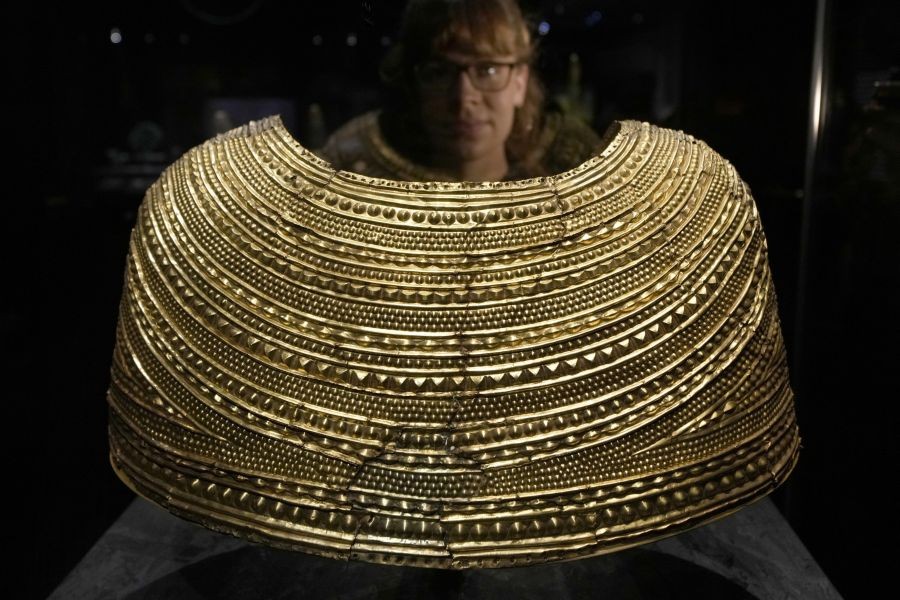 London:  A member of staff poses next to a gold cape found in Mold in Wales, dated 1600-1900 BCE, on display at the The World of Stonehenge' exhibition at the British Museum in London, Monday, Feb. 14, 2022. The exhibition which displays objects and artifacts from the era of Stonehenge opens on Feb. 17 and runs until  July 17, 2022.  AP/PTI