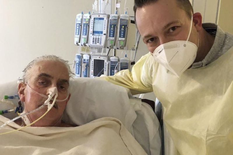 In this photo provided by the University of Maryland School of Medicine, David Bennett Jr., right, stands next to his father's hospital bed in Baltimore, Md., on Jan. 12, 2022, five days after doctors transplanted a pig heart into Bennett Sr., in a last-ditch effort to save his life. Bennett, the first person to receive a heart transplant from a pig died Tuesday, March 8, at the University of Maryland Medical Center, two months after the groundbreaking experiment. His death was announced Wednesday.(AP File Photo)