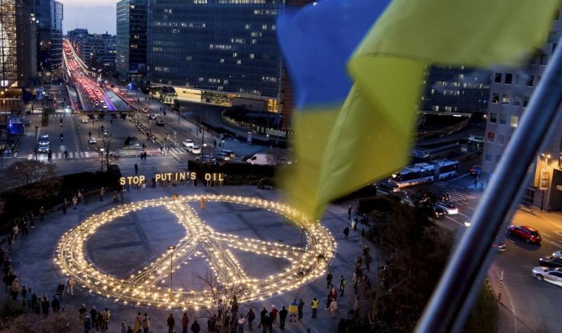People stand around a giant peace sign with the message 'Stop Putin's Oil', put up by demonstrators ahead of an EU and NATO summit in Brussels on March 22. Protestors on Tuesday called on EU leaders to impose a full ban on Russian fuels and to hold one minute of silence to honor the victims of war. (AP Photo)