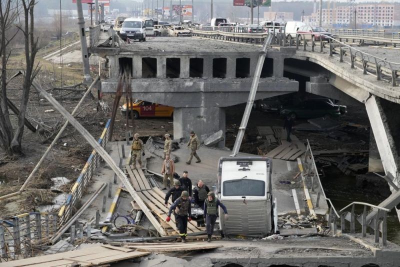 Ukrainian soldiers carry a body of a civilian killed by the Russian forces over the destroyed bridge in Irpin close to Kyiv, Ukraine, Thursday, March 31, 2022. The more than month-old war has killed thousands and driven more than 10 million Ukrainians from their homes including almost 4 million from their country. (AP Photo)