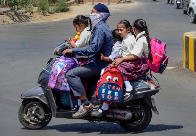 A man shields his face from the heat with a cloth while riding a two-wheeler with children, in Amritsar on April 27, 2022. (PTI Photo)