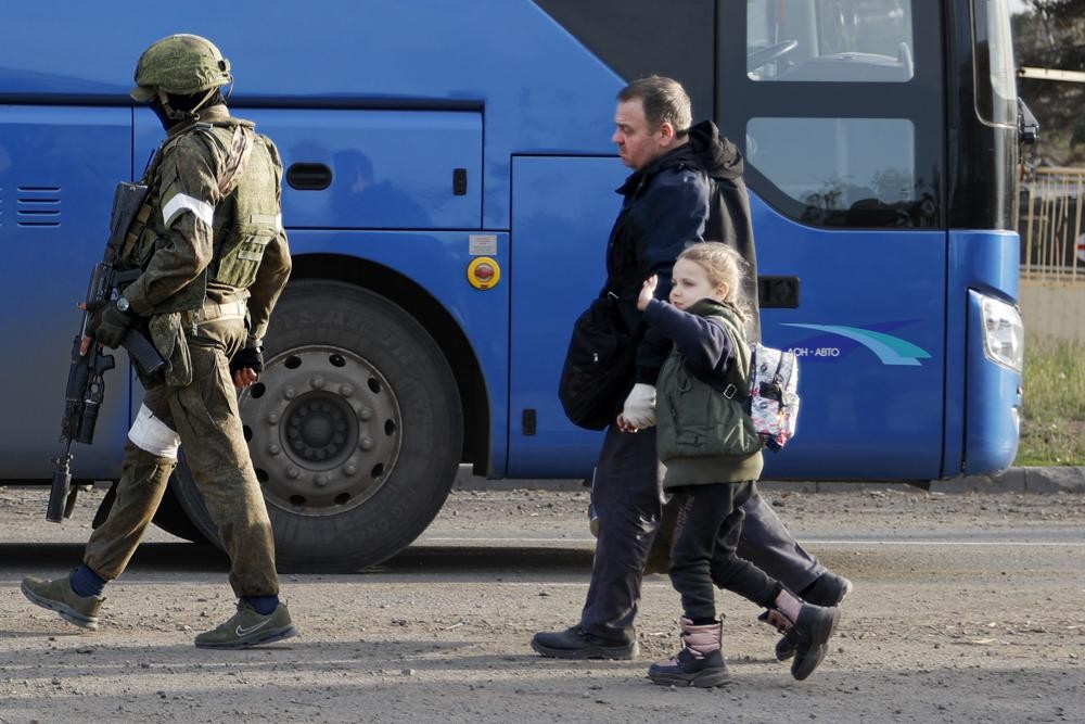 A man and a girl who left a shelter in the Metallurgical Combine Azovstal walk to a bus escorting by a serviceman of Russian Army in Mariupol, in territory under the government of the Donetsk People's Republic, eastern Ukraine, Friday, May 6, 2022. (AP Photo/Alexei Alexandrov)