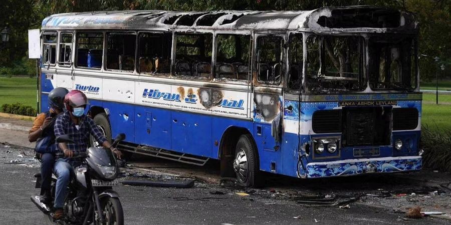A Sri Lankan motorist rides past a burnt bus a day after clashes between government supporters and anti-government protesters in Colombo, Sri Lanka. (Photo | AP)