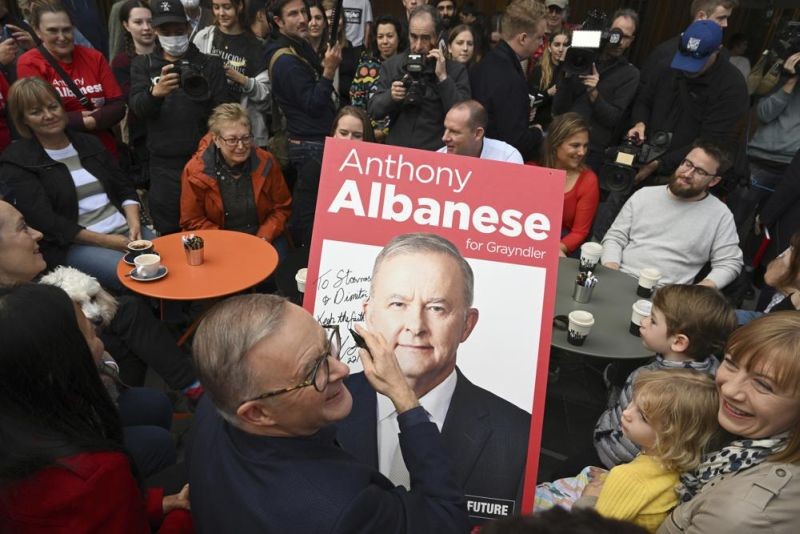 Australia's Prime Minister-elect Anthony Albanese, center, signs a poster for twin brothers Dimitri and Stavros, bottom right, as he visits a coffee shop in suburban Marrickville, Sydney on May 22, 2022. Albanese has promised to rehabilitate Australia's international reputation as a climate change laggard with steeper cuts to greenhouse gas emissions. (AP Photo)