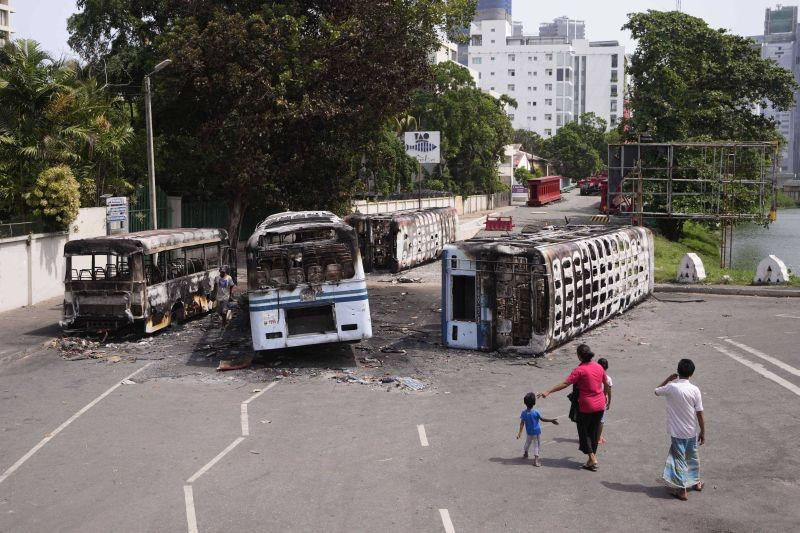 A Sri Lankan family watches the wreckage of buses burnt in clashes in Colombo, Sri Lanka on May 11, 2022. Sri Lanka's defense ministry ordered security forces on Tuesday to shoot anyone causing injury to people or property to contain widespread arson and mob violence targeting government supporters.  (AP/PTI Photo)