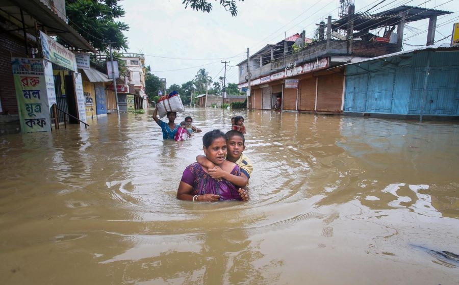 Agartala: A woman carries a child through a flooded area after heavy rains, on the outskirts of Agartala, Saturday, June 18, 2022. (PTI Photo)
