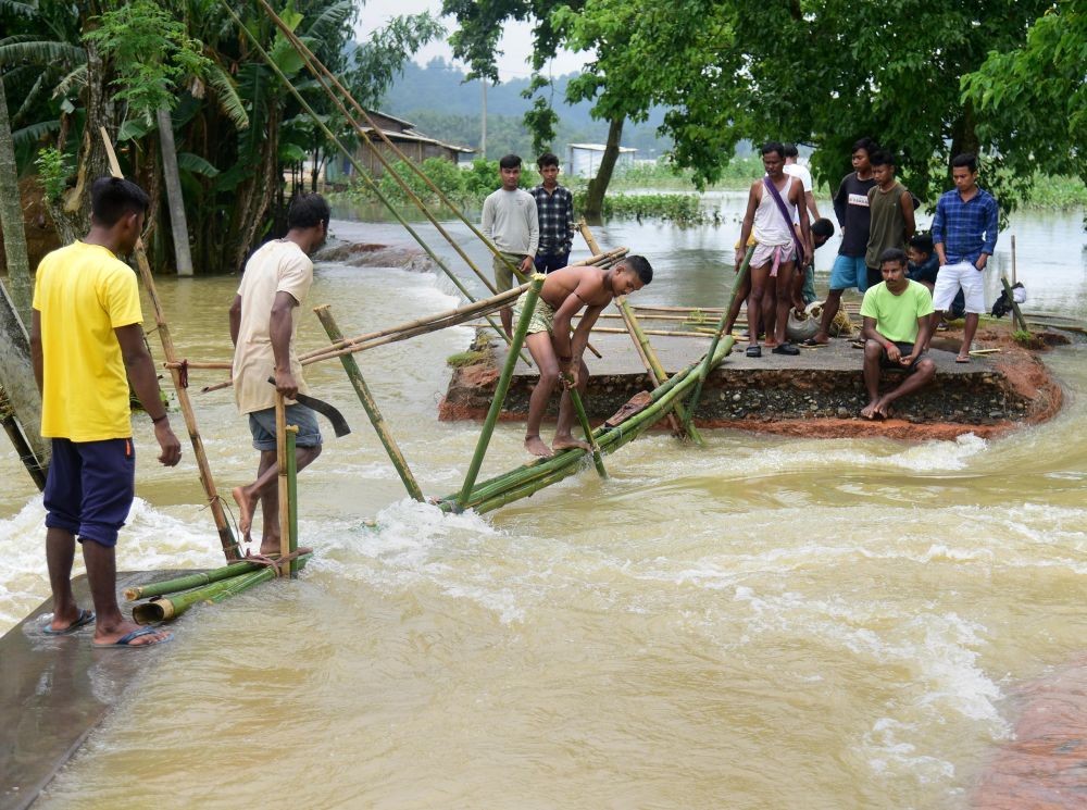 Goalpara: Villagers make a temporary bamboo bridge after a portion of a road was washed away by the flood water at a village in Goalpara district of Assam state, Saturday, June 18 2022.  (PTI Photo)