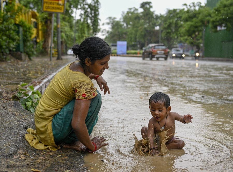 New Delhi: A woman keeps a watch on her child who plays on a waterlooged road amid monsoon rains, in New Delhi, Saturday, July 16, 2022. (PTI Photo/Arun Sharma)