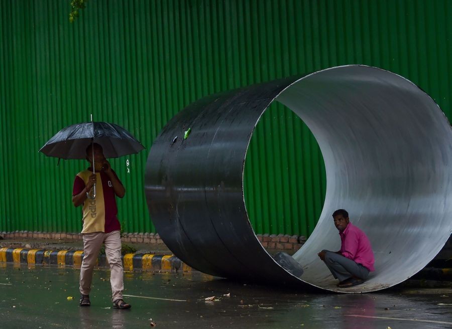 EDS PLS TAKE NOTE OF THIS PTI PICK OF THE DAY:::New Delhi: A man holding umbrella walks as another sits inside a pipe amid monsoon rains, in New Delhi, Saturday, July 16, 2022. (PTI Photo/Manvender Vashist Lav)