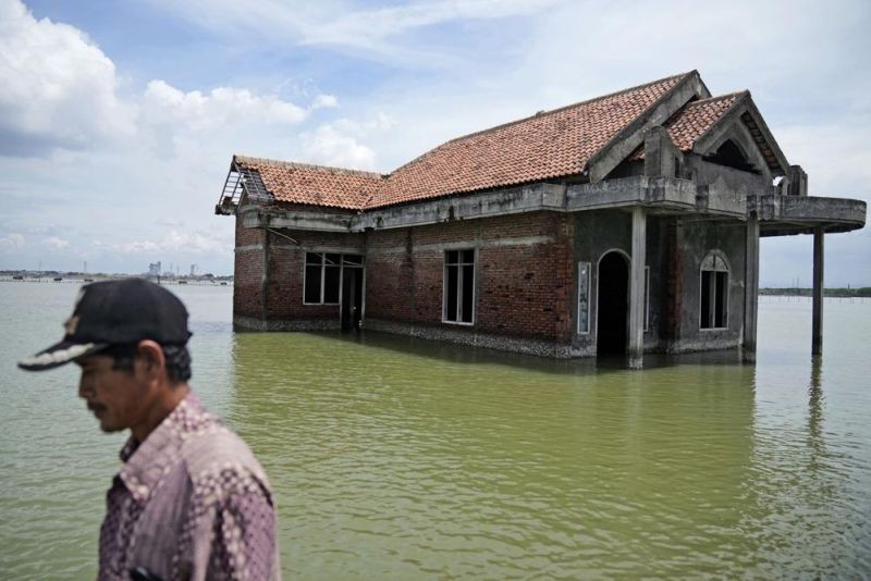 A man walks past a house abandoned after it was inundated by water due to the rising sea level in Sidogemah, Central Java, Indonesia. (AP File Photo)